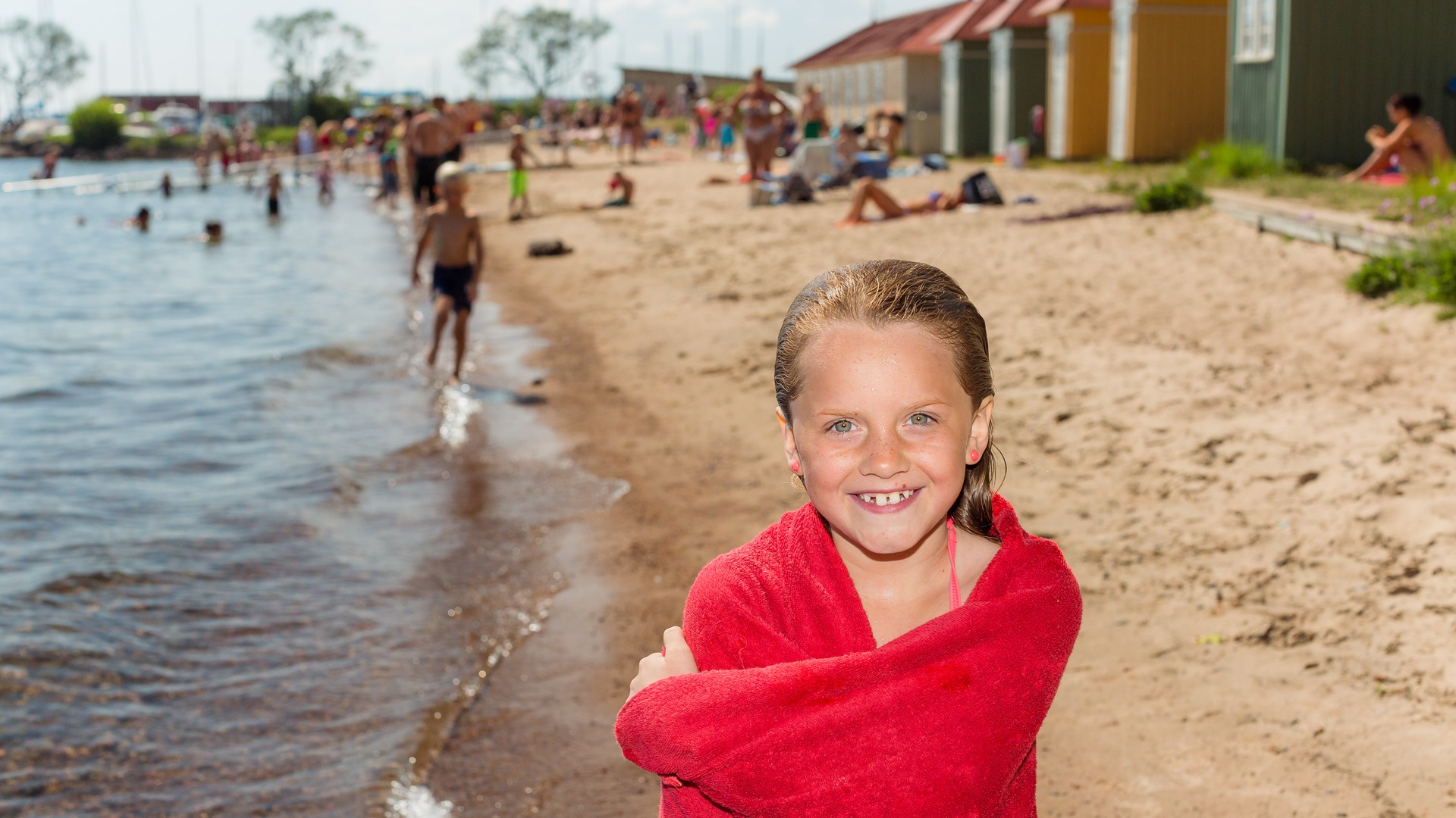 Ung tjej i handduk står på stranden vid Guldkroksbadet och ler in i kameran.