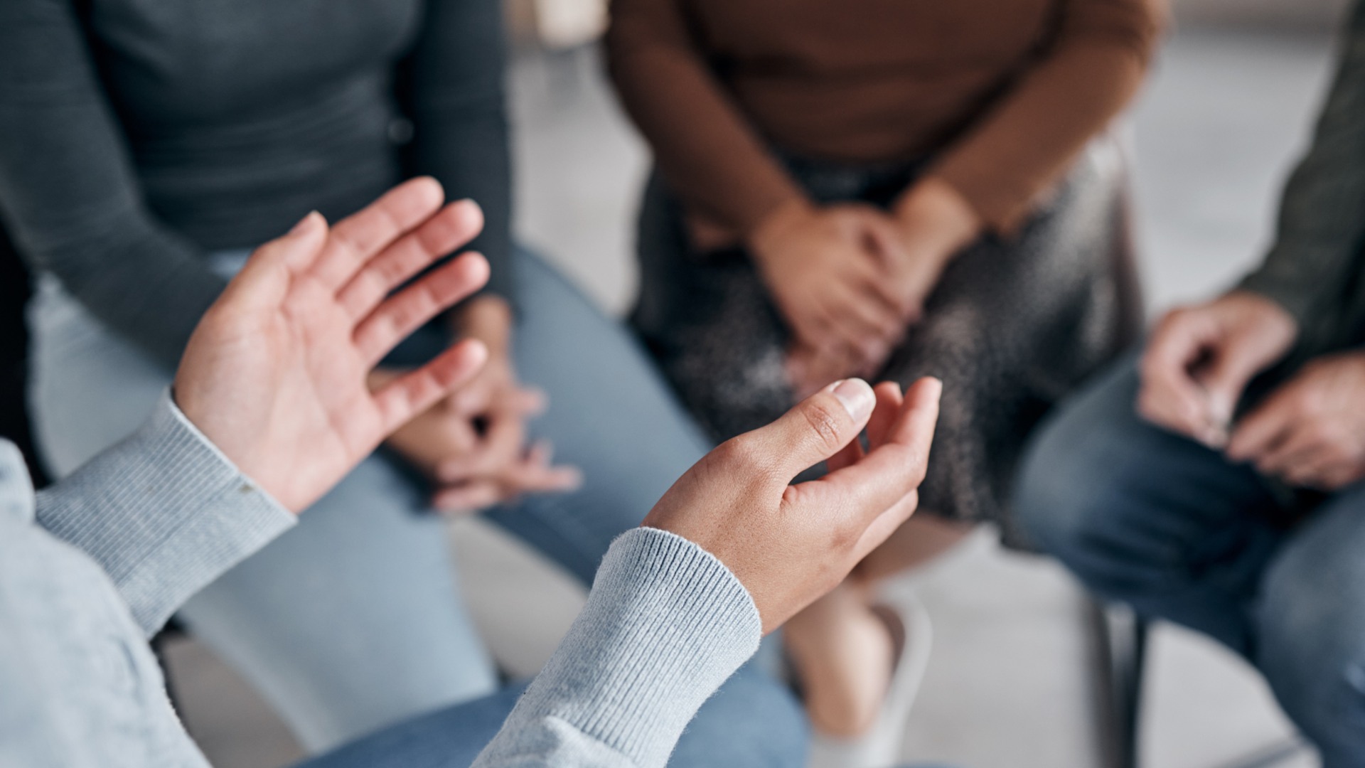 Personer sitter på stolar i en ring. I förgrunden syns en persons händer som gestikulerar.