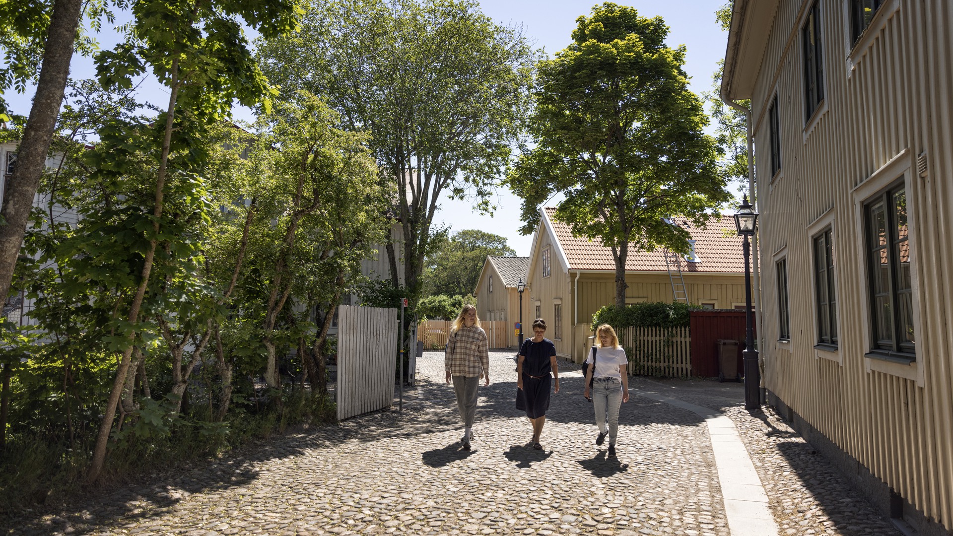 Tre personer promenerar på en kullerstensgata i Hjo.