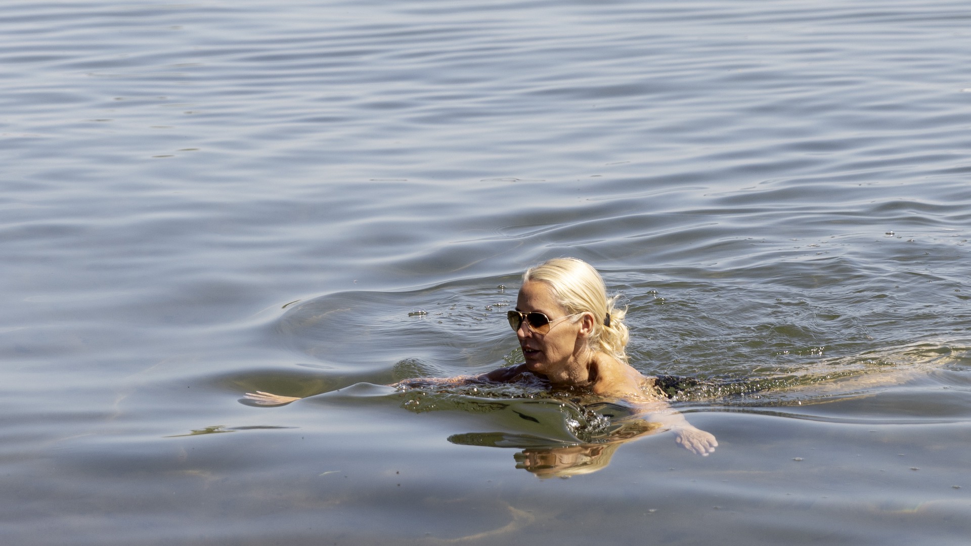 En person simmar i Vättern. Hamnen syns i horisonten.