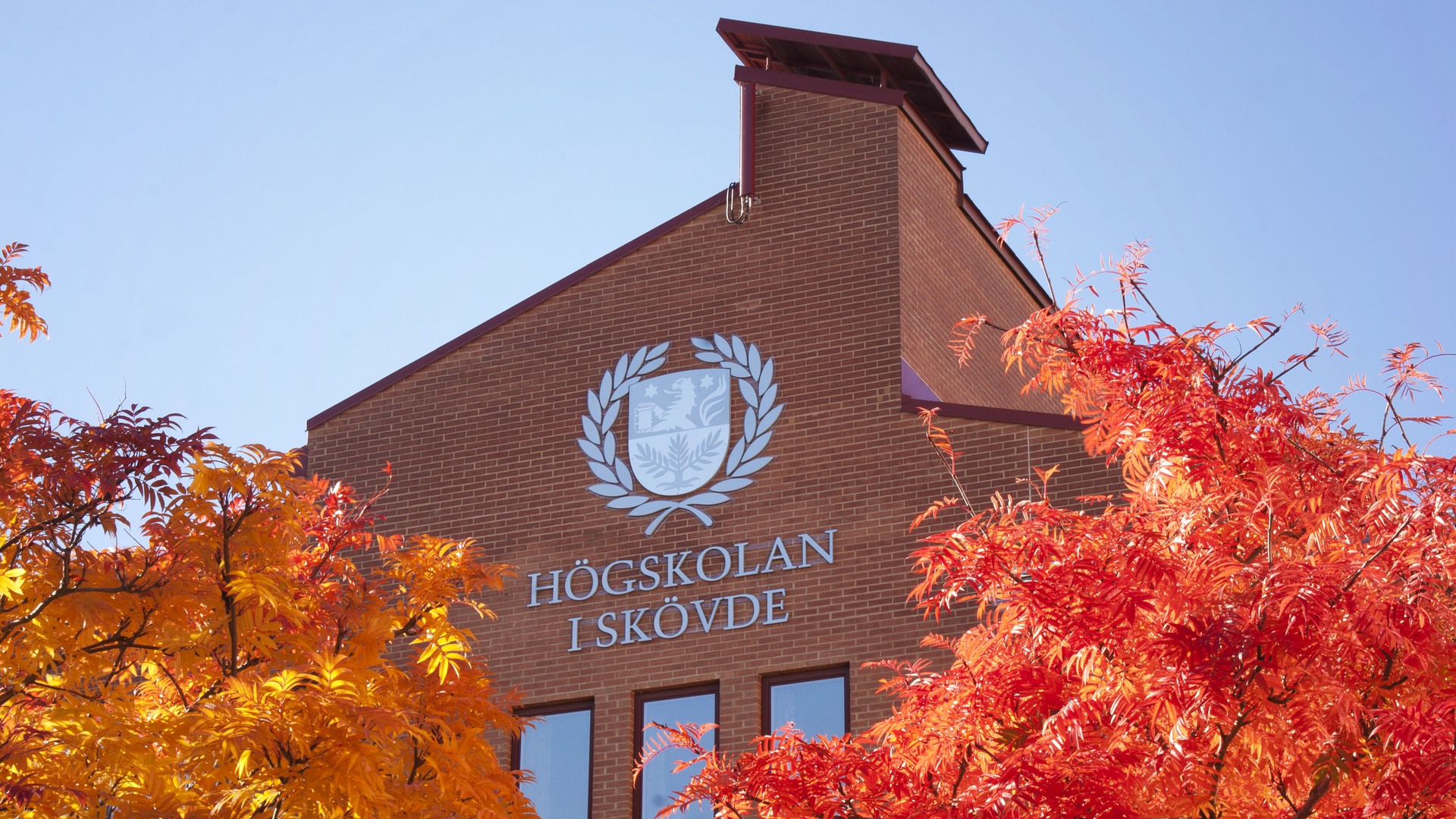 Högskolan i Skövde exteriör med höstlöv framför.