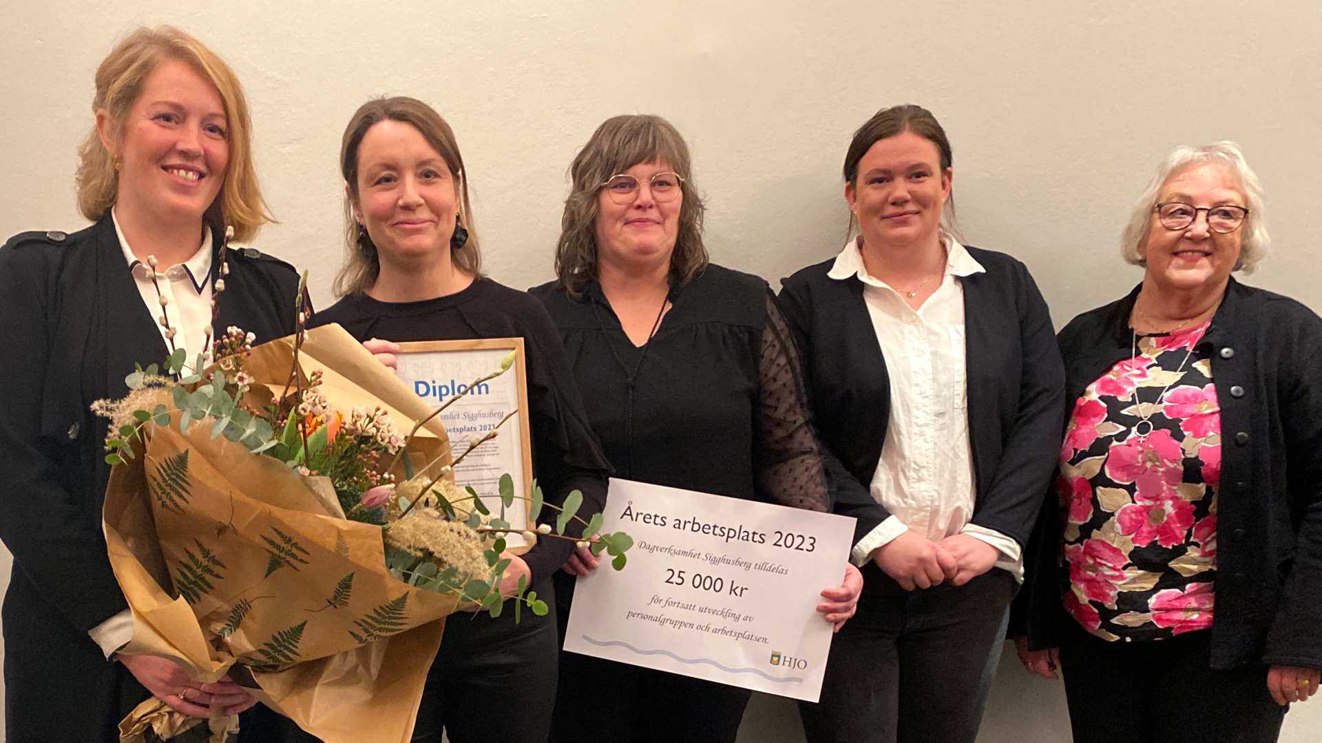 Gruppbild på dagverksamhetens personal med blommor, diplom och stipendiecheck i händerna.