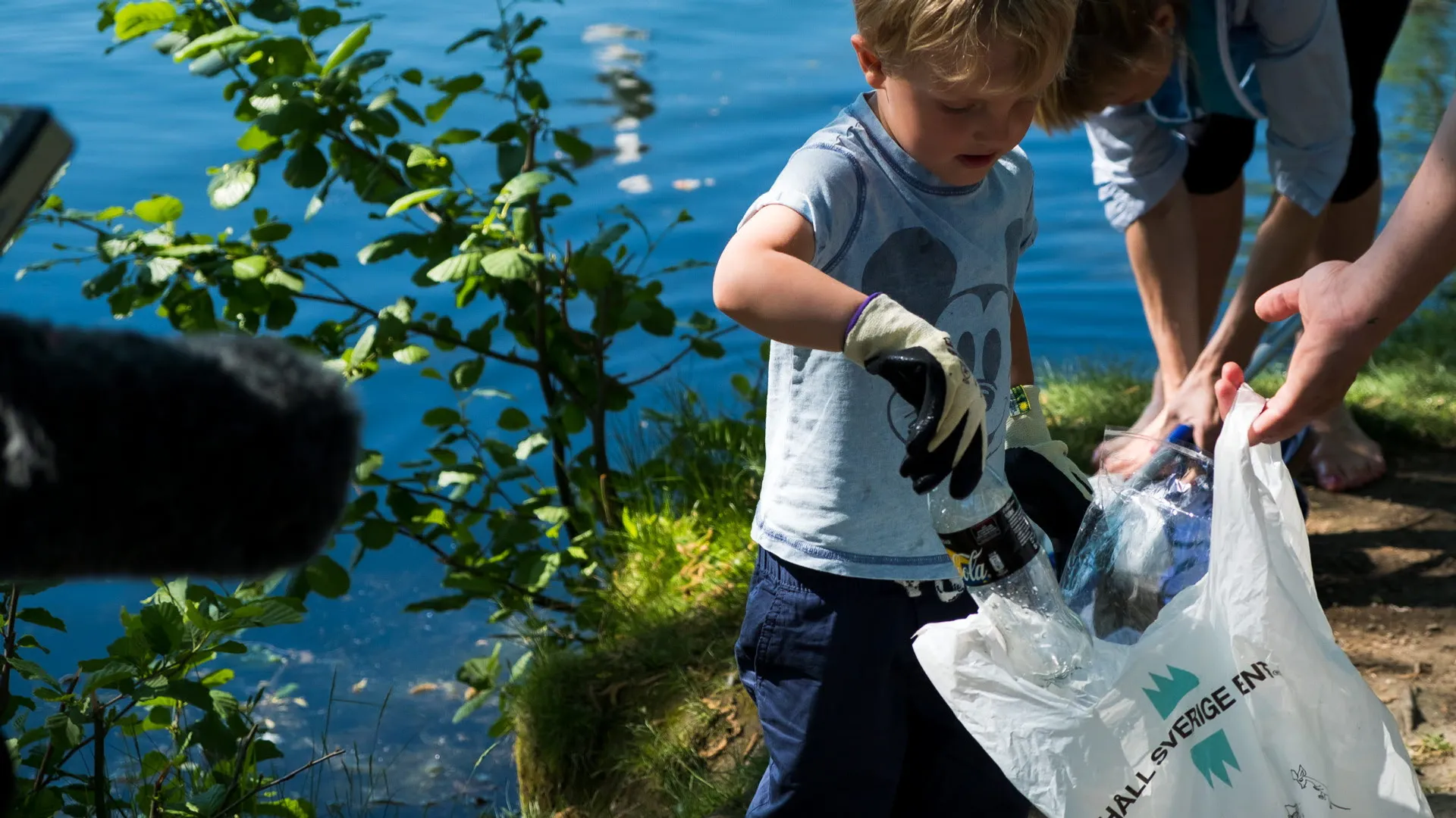 Ett barn plockar skräp i en plastpåse med texten "Håll Sverige rent" 