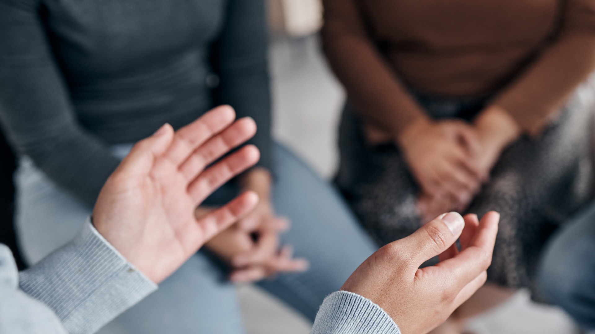 Personer sitter på stolar i en ring. I förgrunden syns en persons händer som gestikulerar.