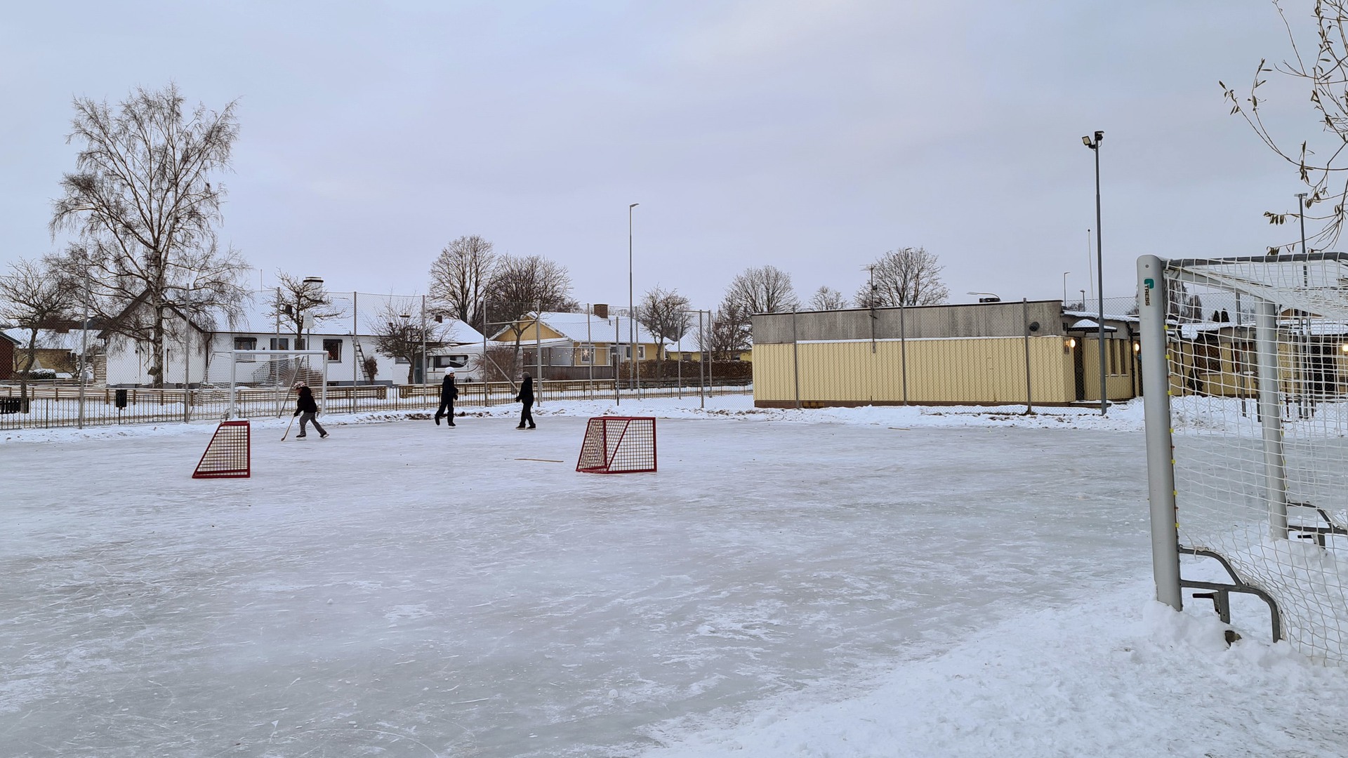 Tre barn åker skridskor på spolad is utanför Guldkroksskolan.