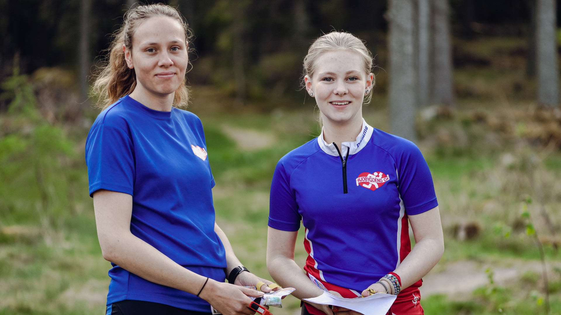 Två personer i skogen med varsin orienteringskarta.