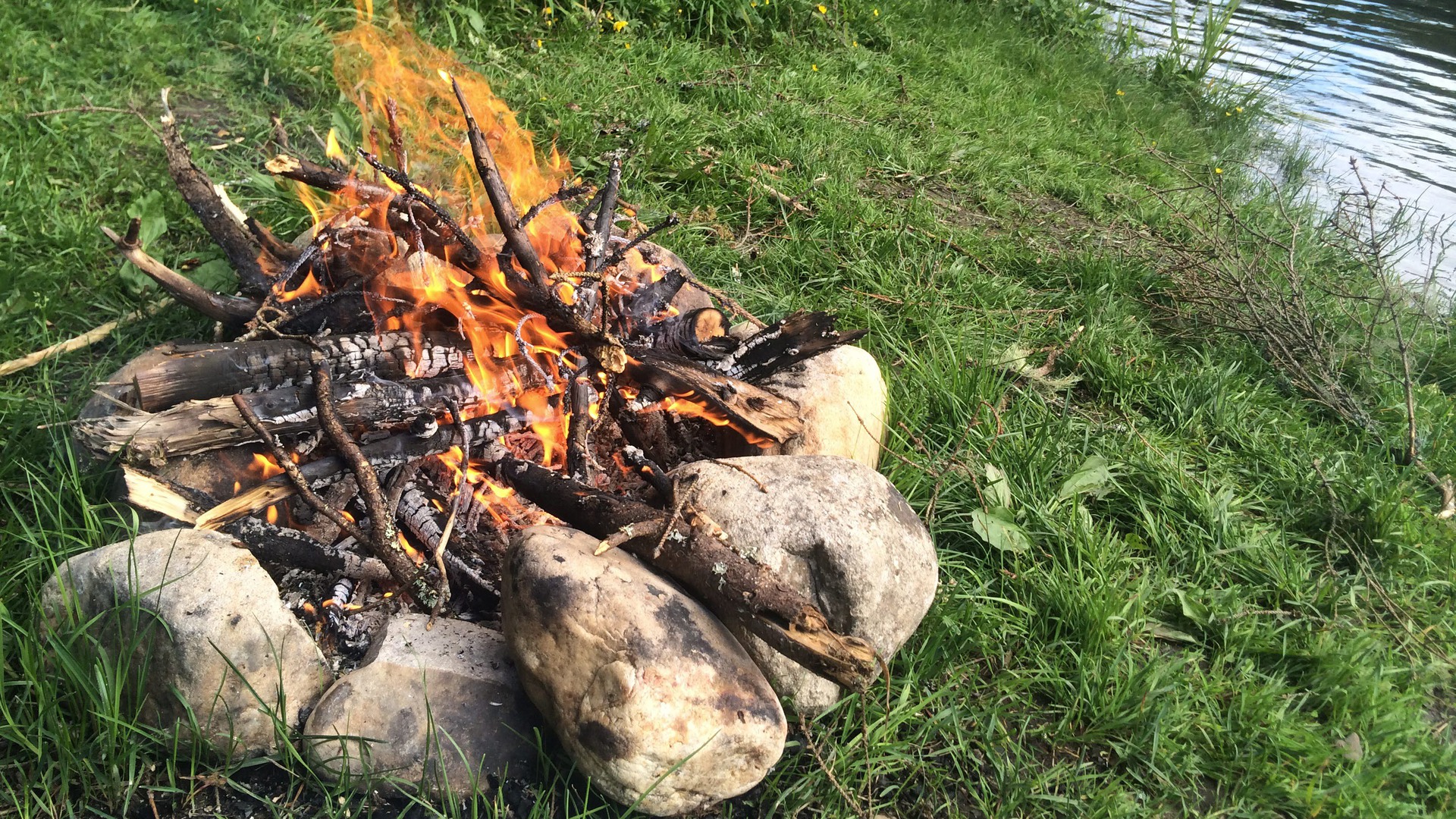 En öppen eld i naturen, med stenar runt omkring.