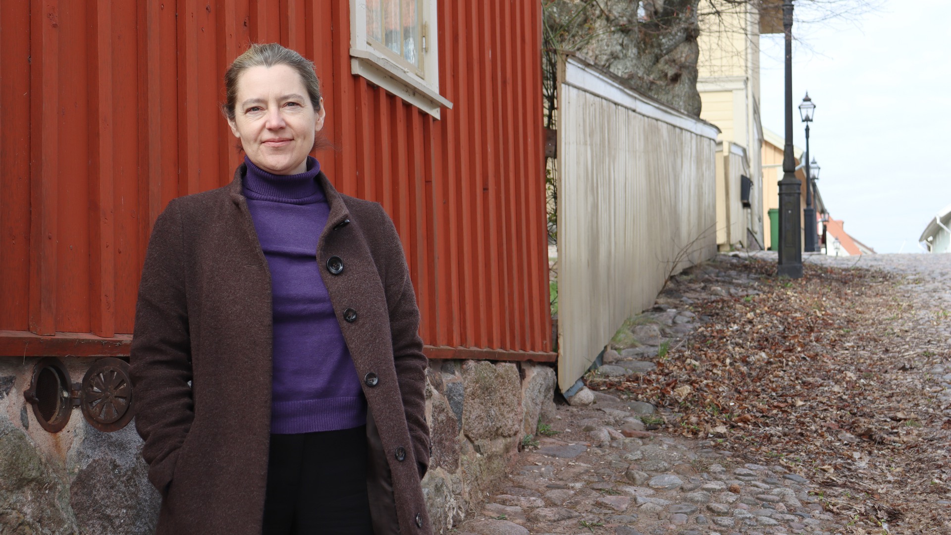 Matilda Åslin står på kullersten vid en röd träfasad.