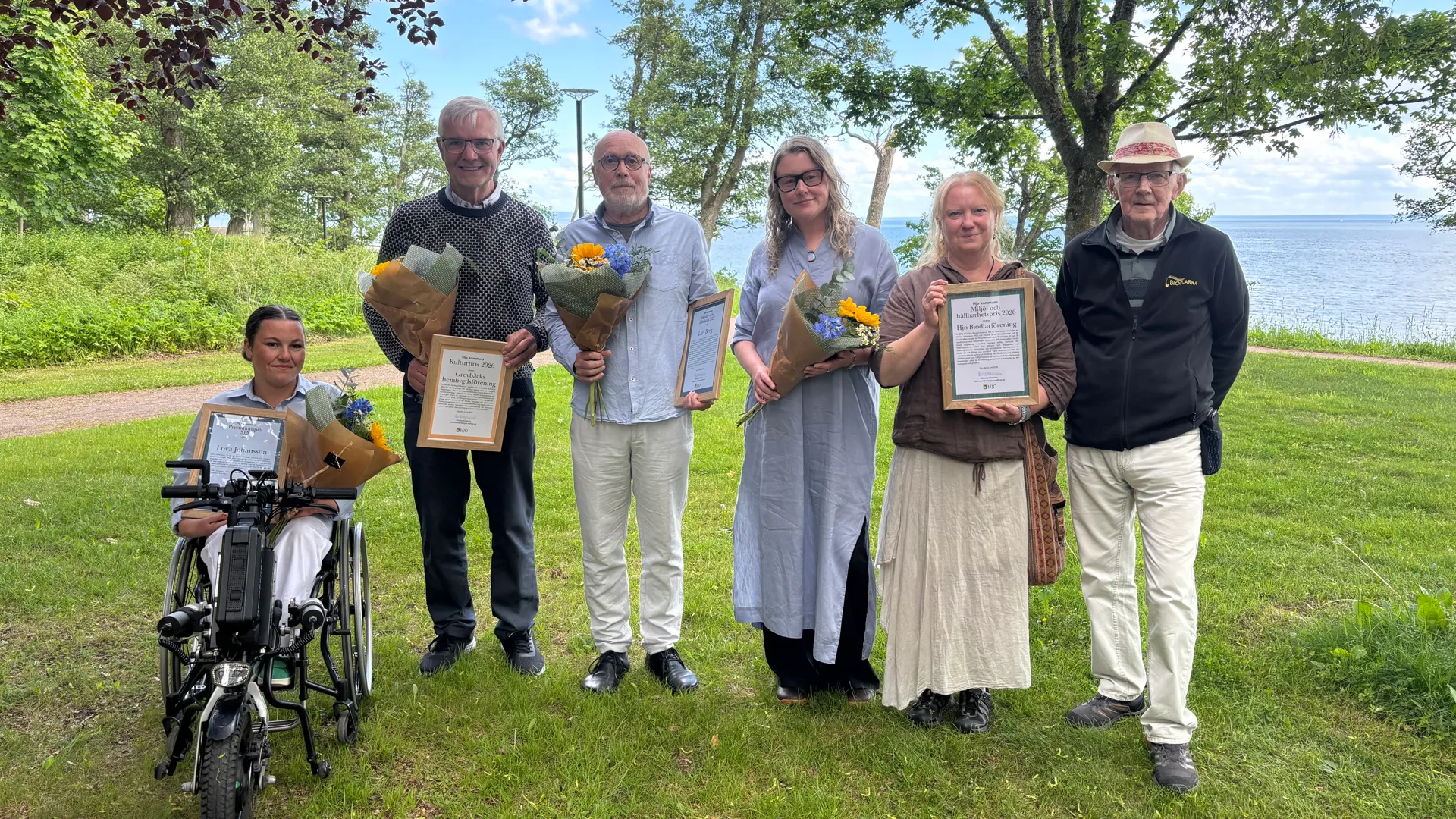 Årets pristagare står på rad framför Vättern och håller upp diplom och blommor.