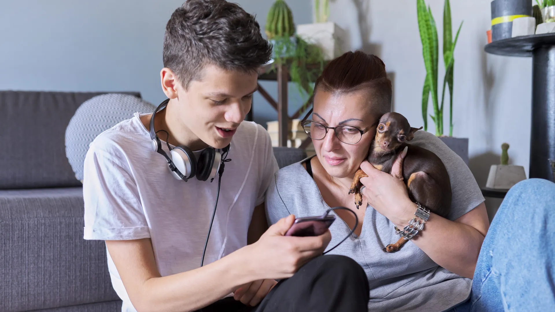 En son och en mamma kollar på något på sonens telefon. Mamman håller i en hund.