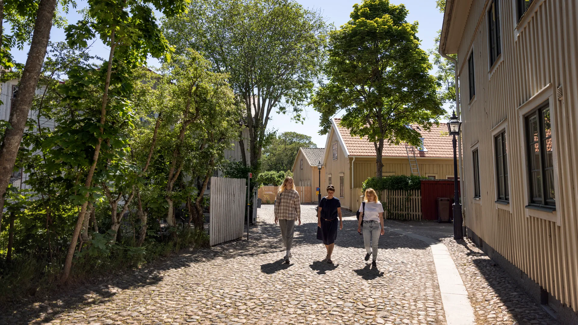 Tre personer promenerar på en kullerstensgata i Hjo.
