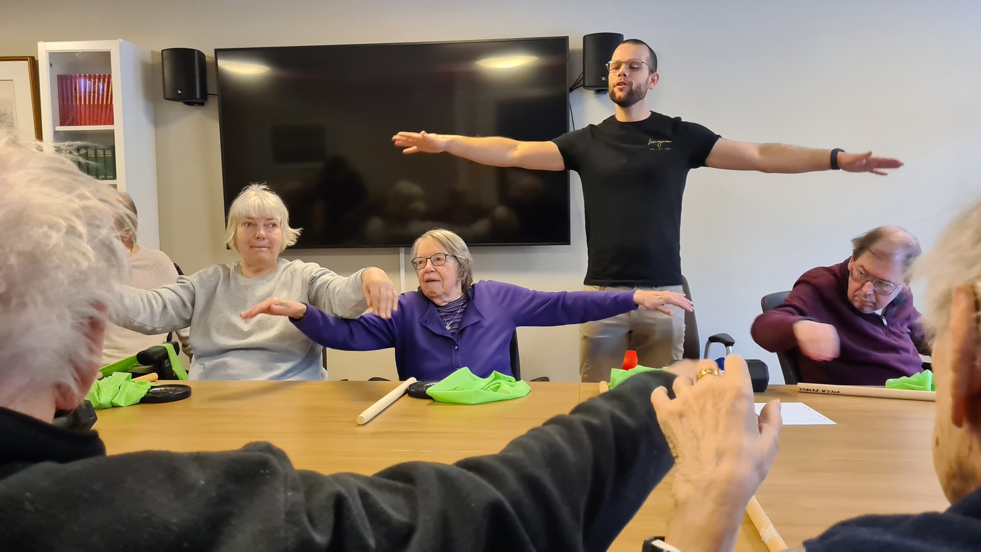 Gymmet Livingroom håller träningspass på Villa Rosell. Boende sitter runt ett bord och utför träningsövningar.