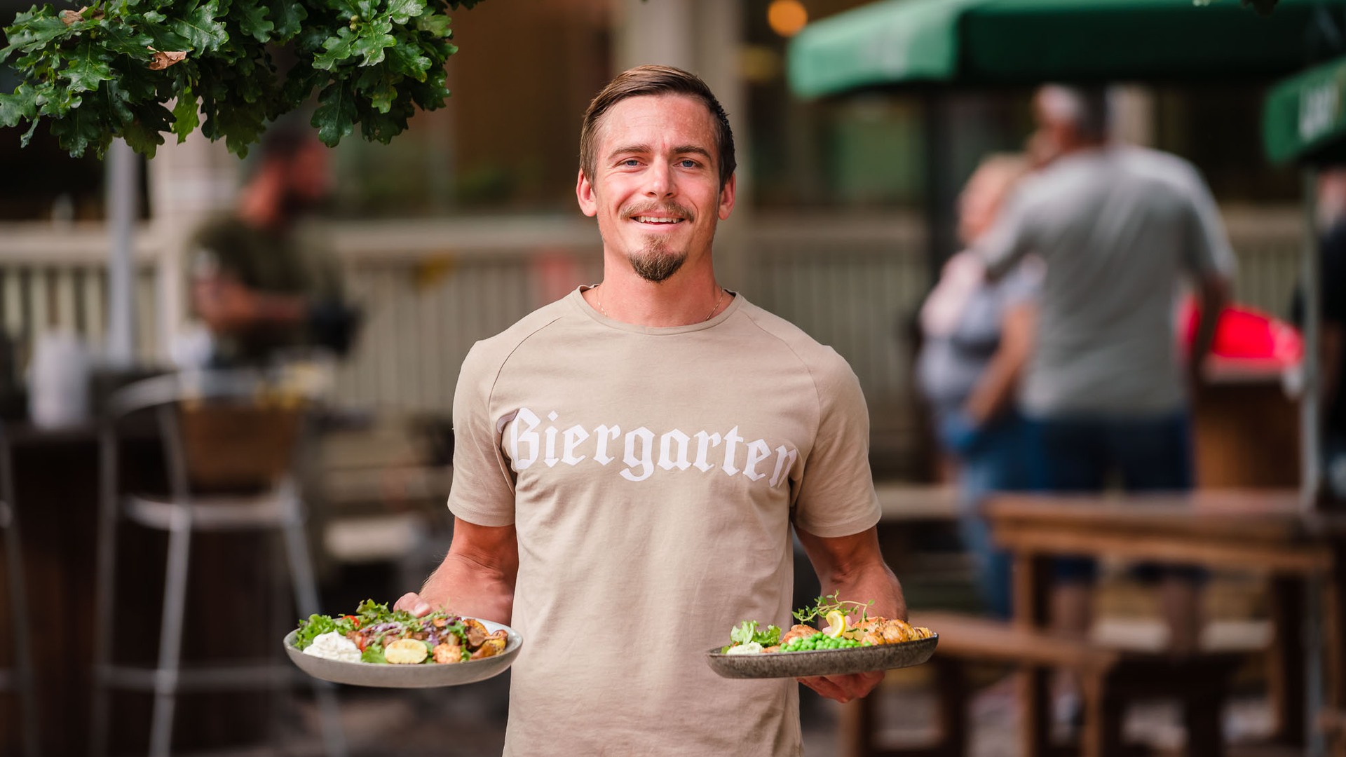 Personal på Biergarten serverar två tallrikar med mat i trädgården. 