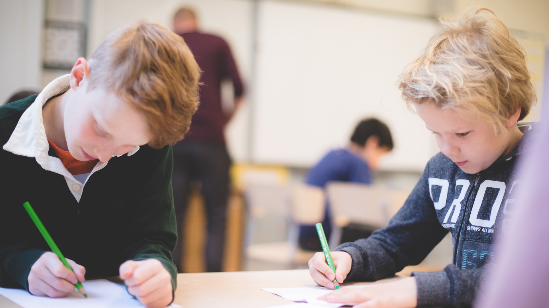 Två elever sitter i klassrummet och antecknar i en skrivbok.