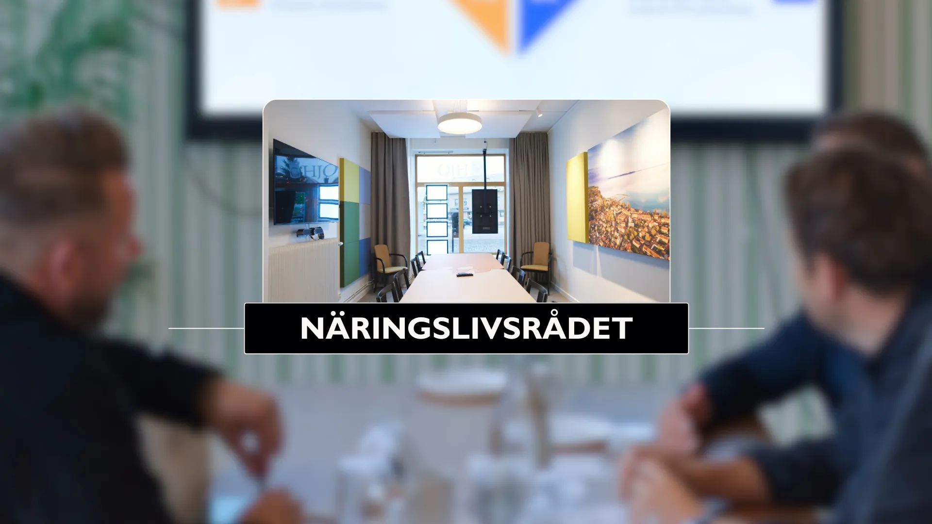 Två män sitter vid ett bord framför en skärm.