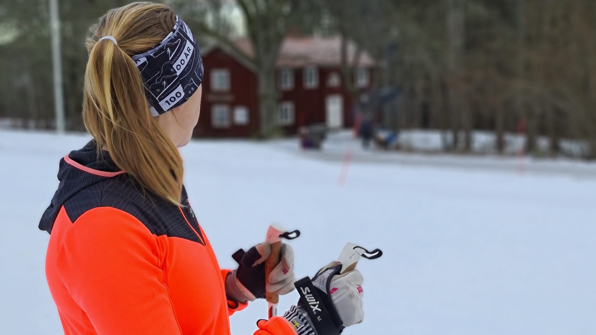 Skidåkare i orange jacka på Högaliden. I bakgrunden syns en röd stuga och det är snö på marken.