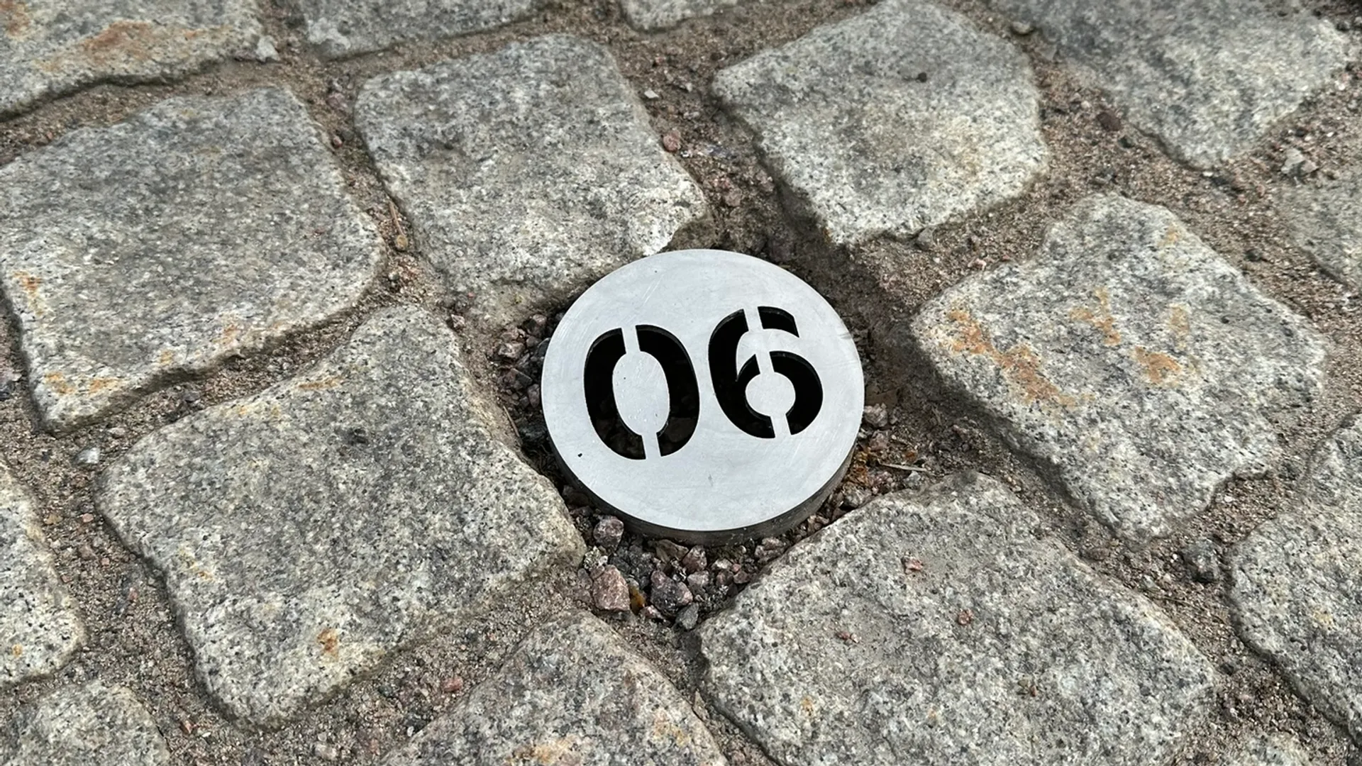 En vit och svart skylt som sitter på toppen av en kullerstensväg.