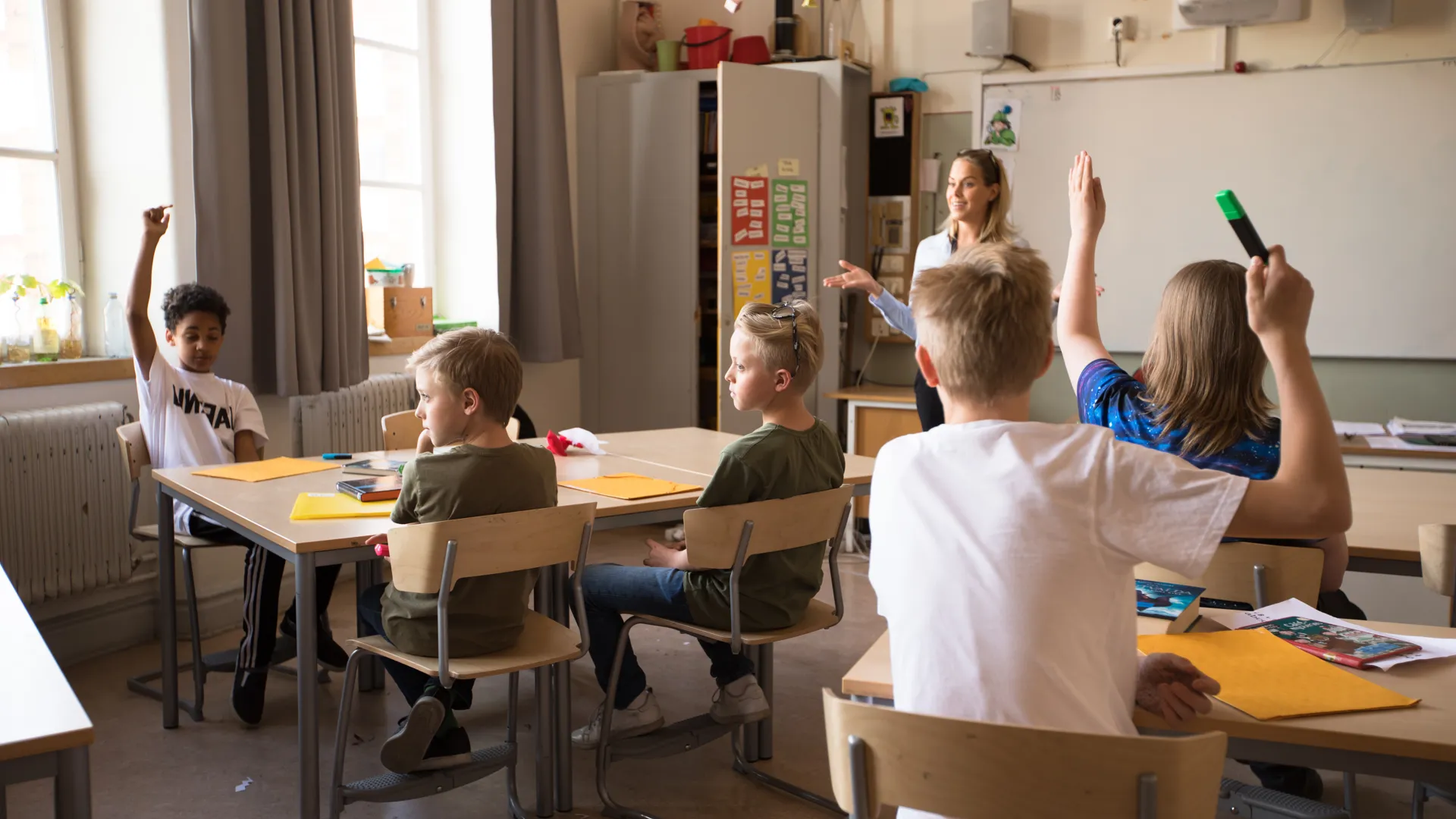 Fler elever räcker upp handen i klassrummet.