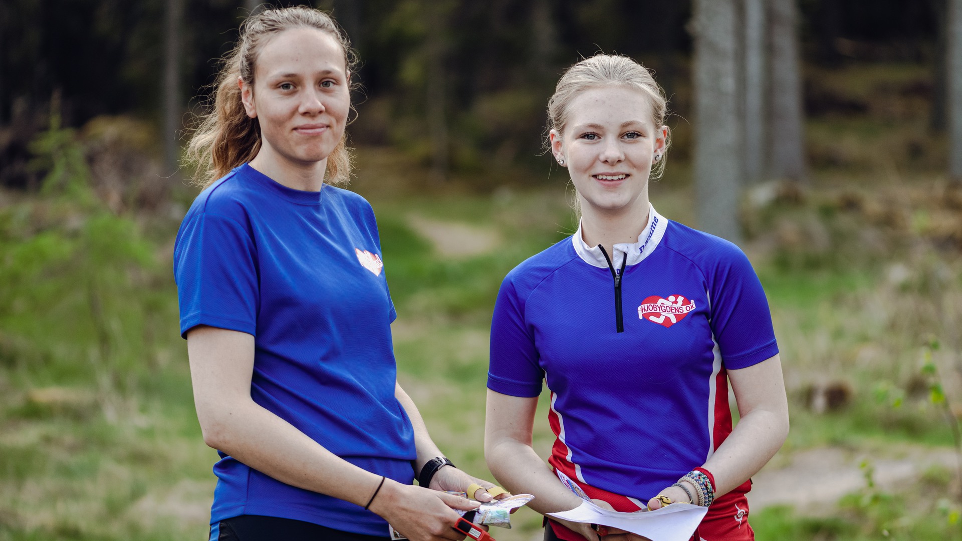 Två personer i skogen med varsin orienteringskarta.