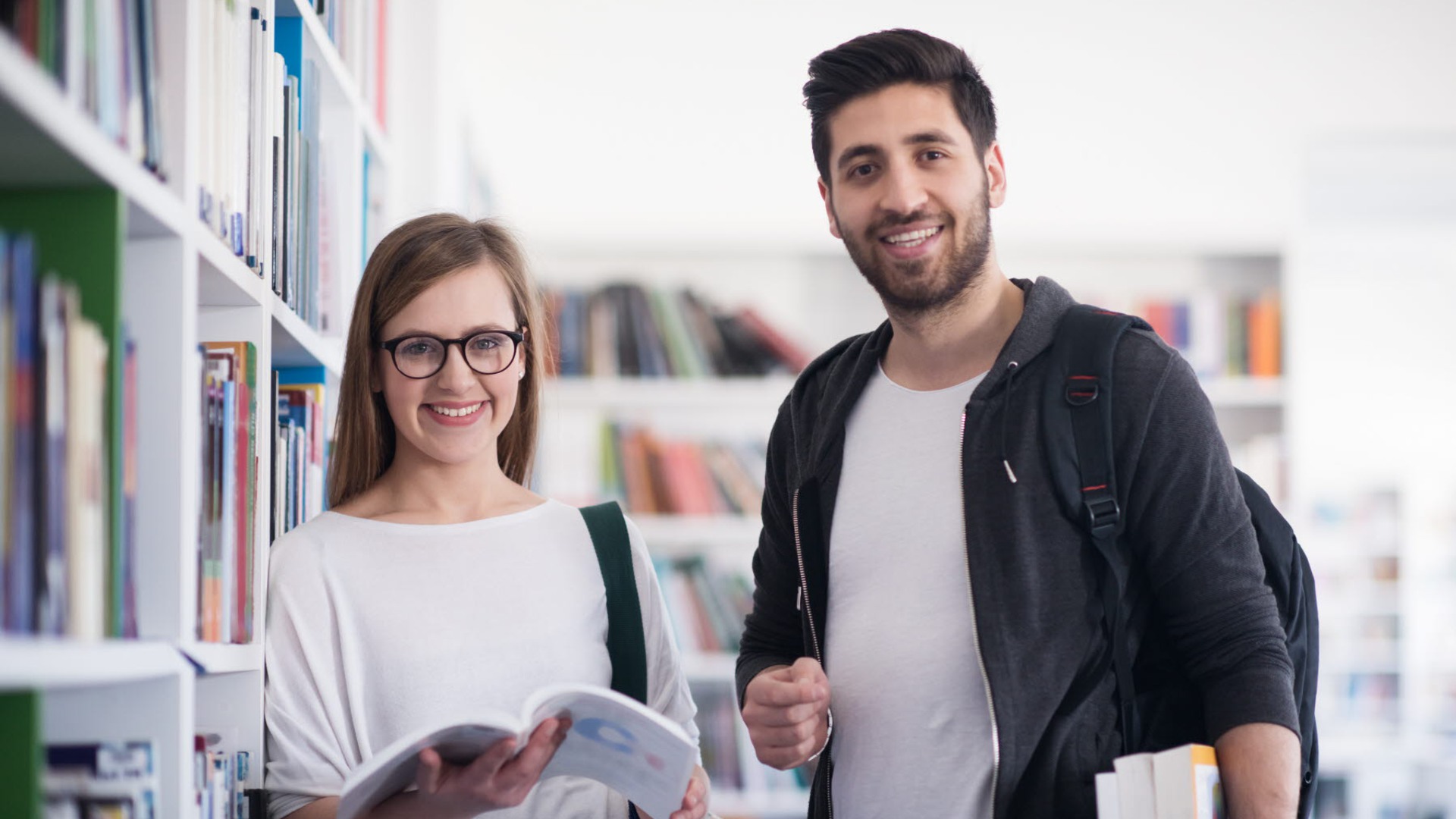 Två personer står i ett bibliotek och håller i böcker.