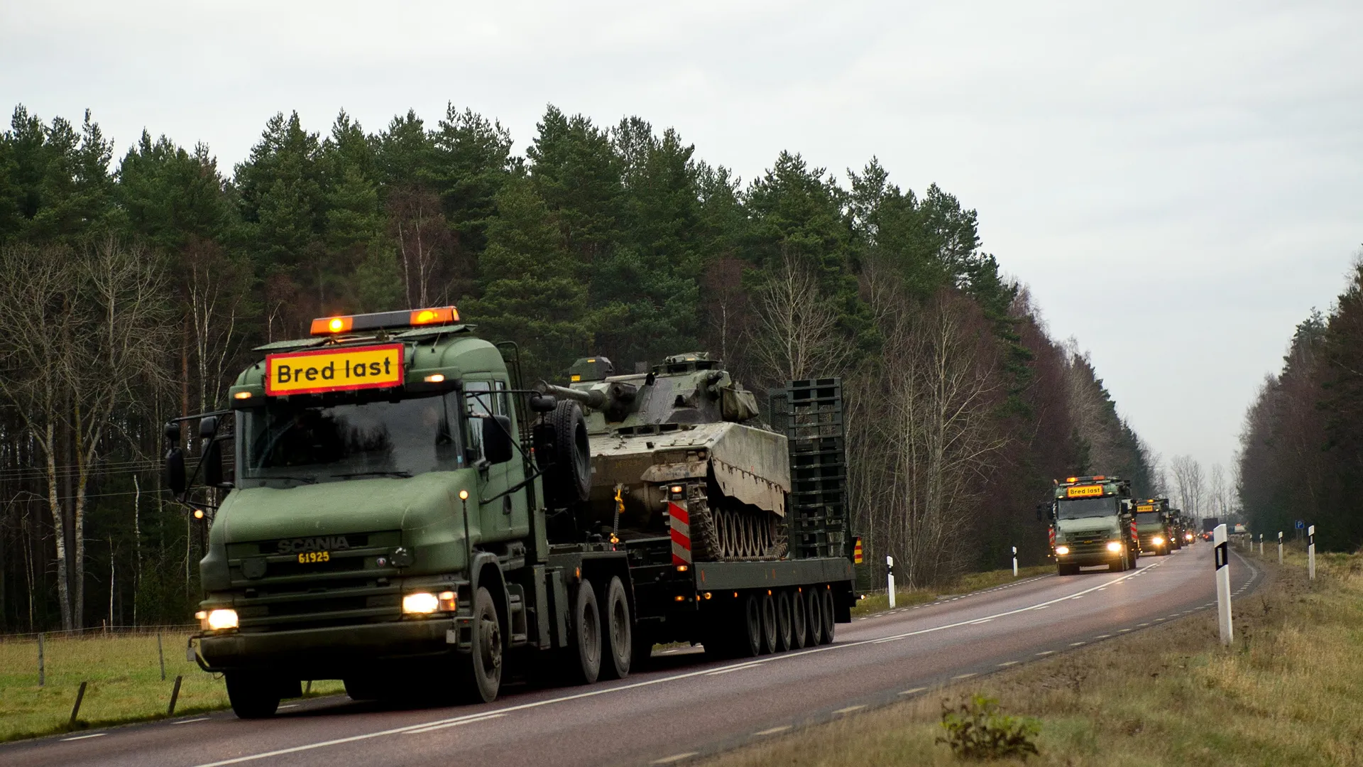 Militärlastbil med stridsvagn på släp kör på allmän väg.