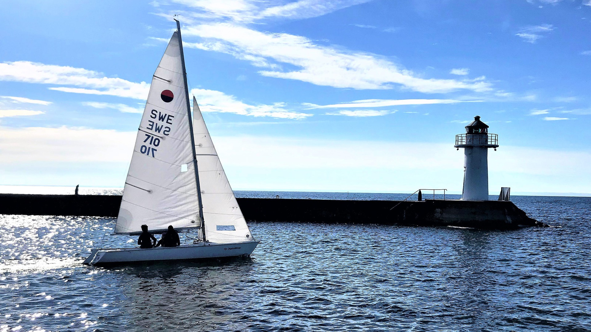 Segelbåt som en solig dag seglar ut från Hjo hamn förbi fyren på vågbrytaren