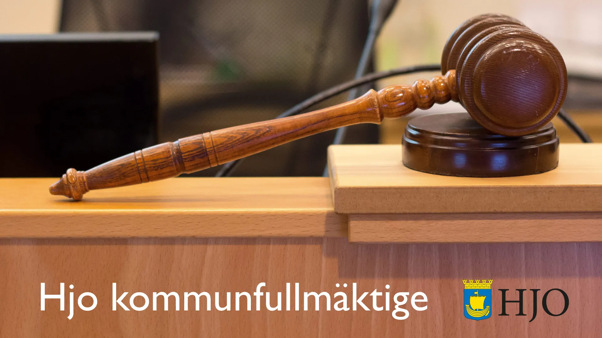 En beslutsklubba på ett bord, samt texten "Hjo kommunfullmäktige".