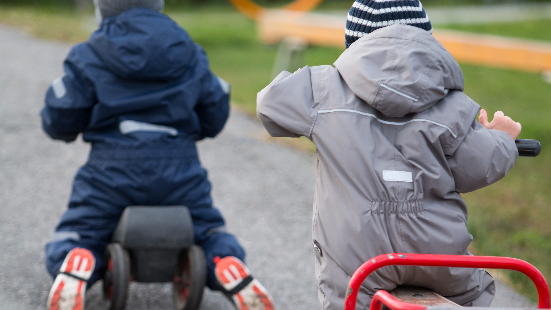 Två förskolebarn cyklar på gården.