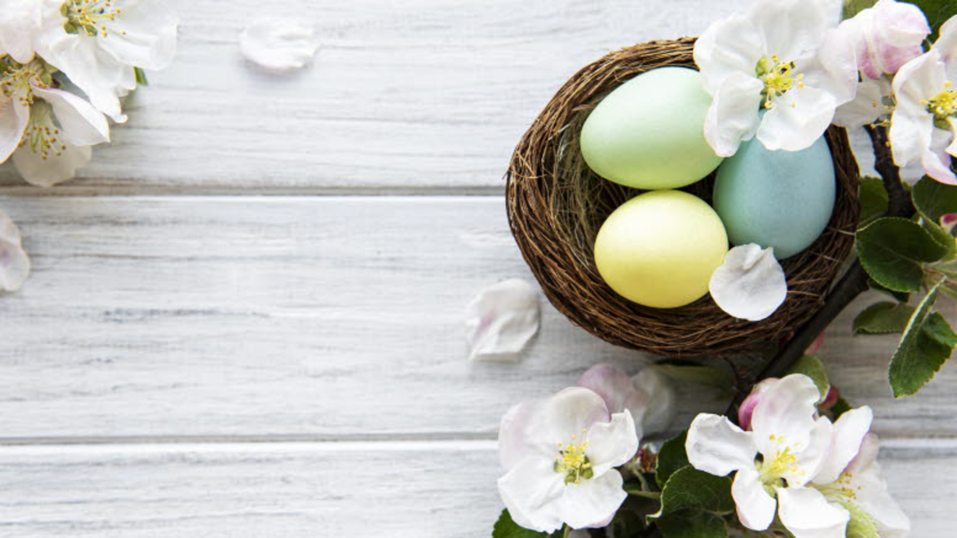 En korg med färgglada ägg och blommor runtomkring.