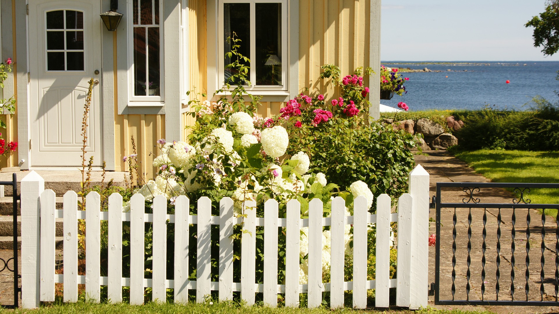 Ett gult trähus vid vattnet, med ett vitt staket framför.