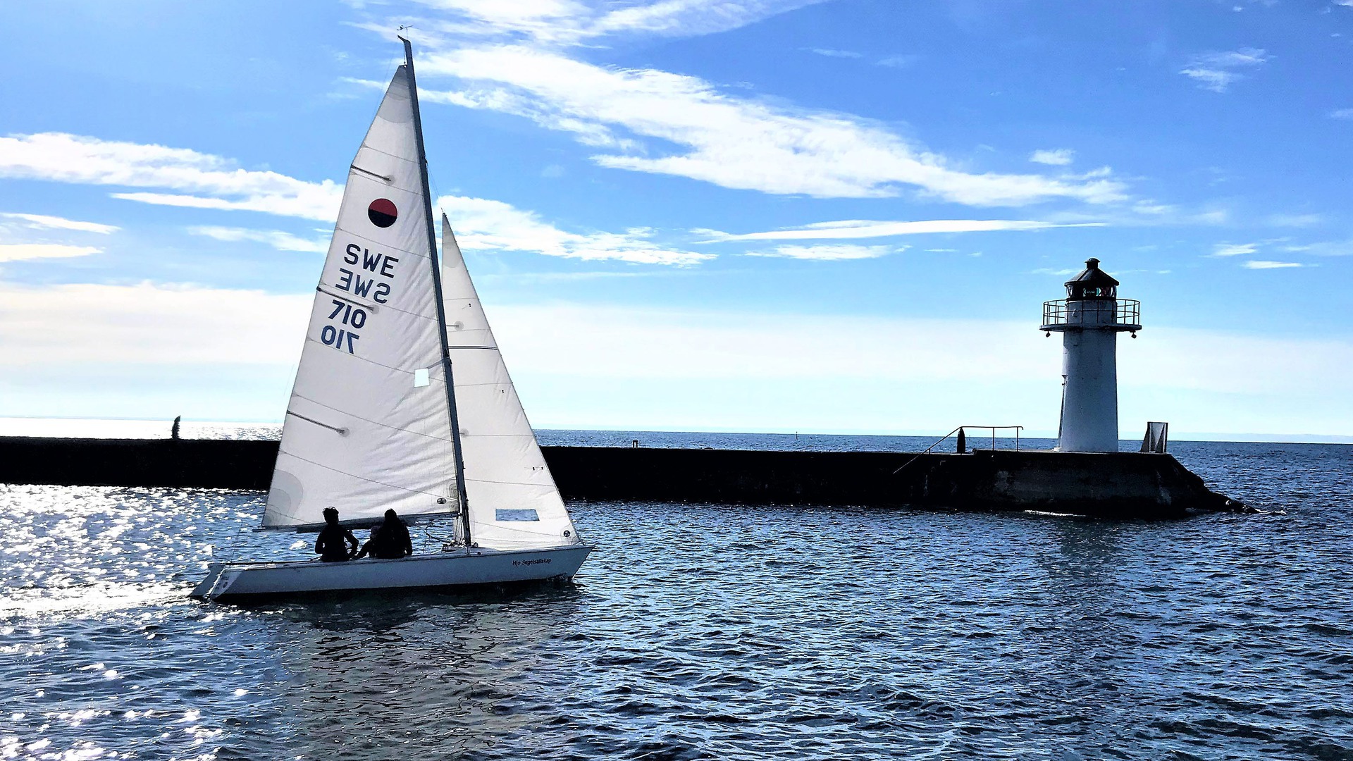 Segelbåt som en solig dag seglar ut från Hjo hamn förbi fyren på vågbrytaren