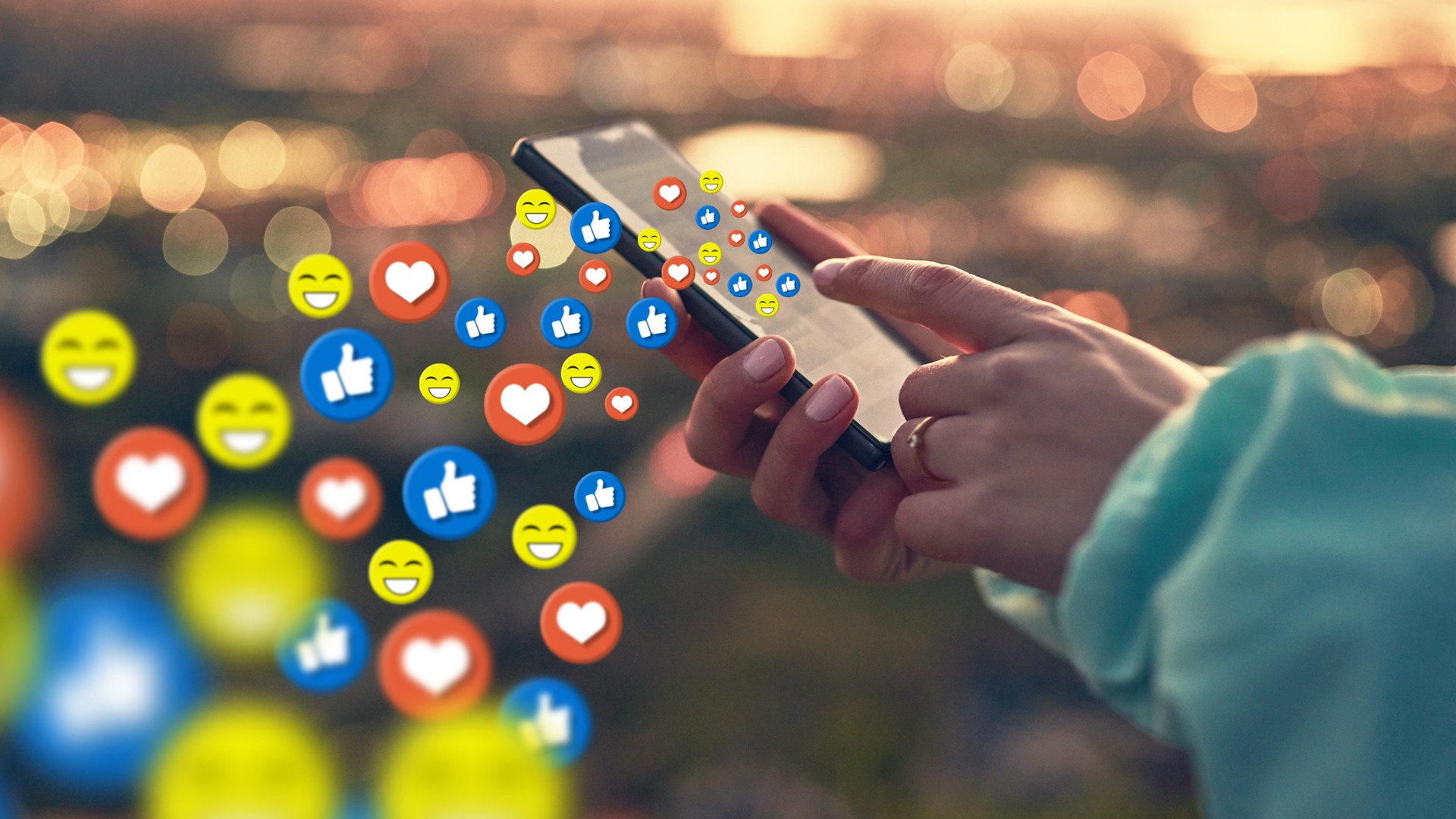 En person håller i en mobiltelefon. Från skärmen strömmar illustrerade sociala medier-ikoner.