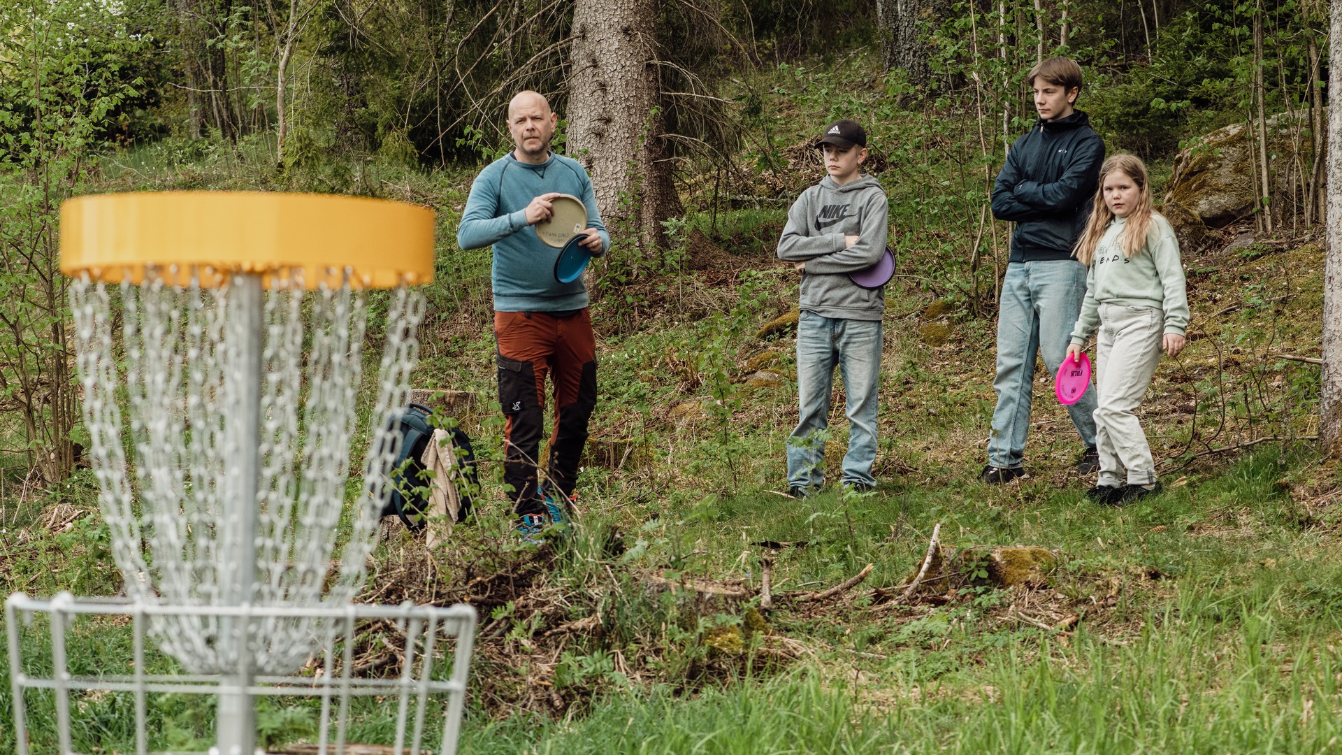 Vuxna och barn vid en korg på discgolfbanan i Högaliden.